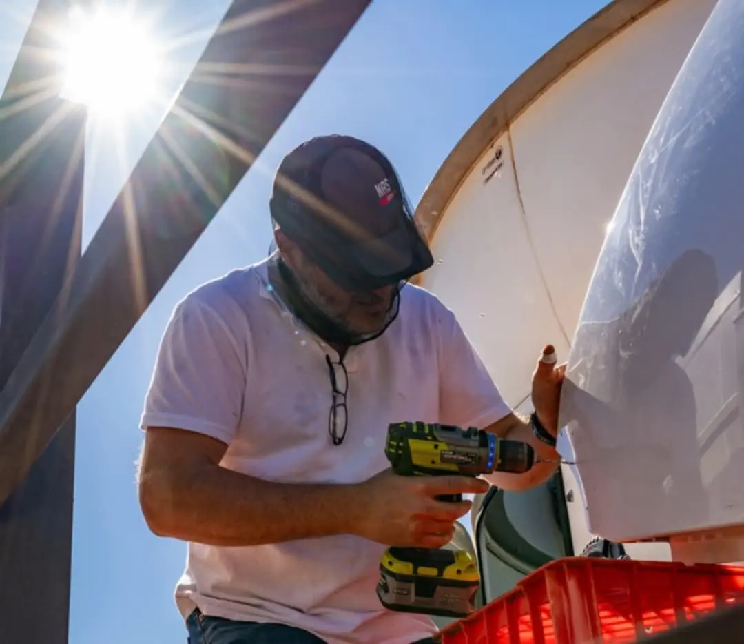 An Astroworx technician working on the dome with a cordless drill, backlit by the sun